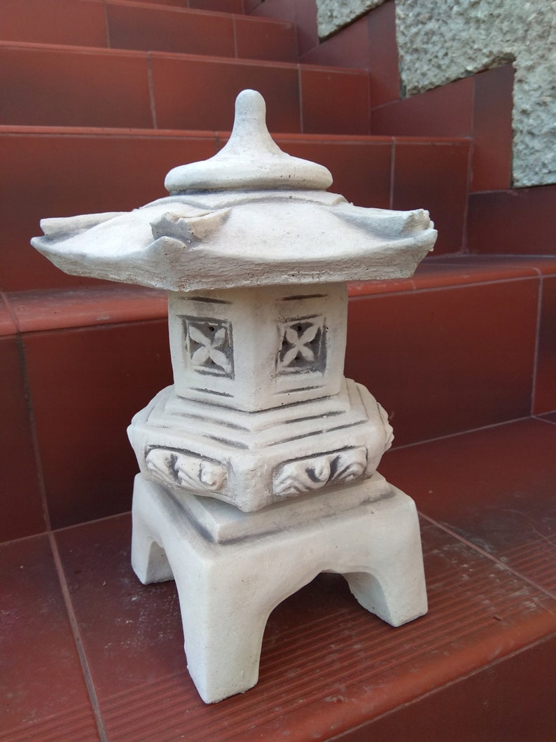 Puede incluir: Una linterna de pagoda de cer&aacute;mica blanca con detalles intrincados y una base cuadrada. La linterna tiene un techo escalonado y recortes decorativos en los lados.