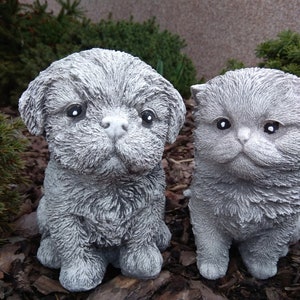 May include: A gray concrete figurine of a dog and a cat sitting side by side. The dog has a fluffy appearance and the cat has a round face.