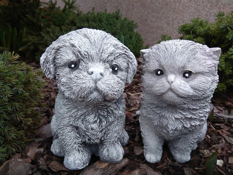 May include: A gray concrete figurine of a dog and a cat sitting side by side. The dog has a fluffy appearance and the cat has a round face.