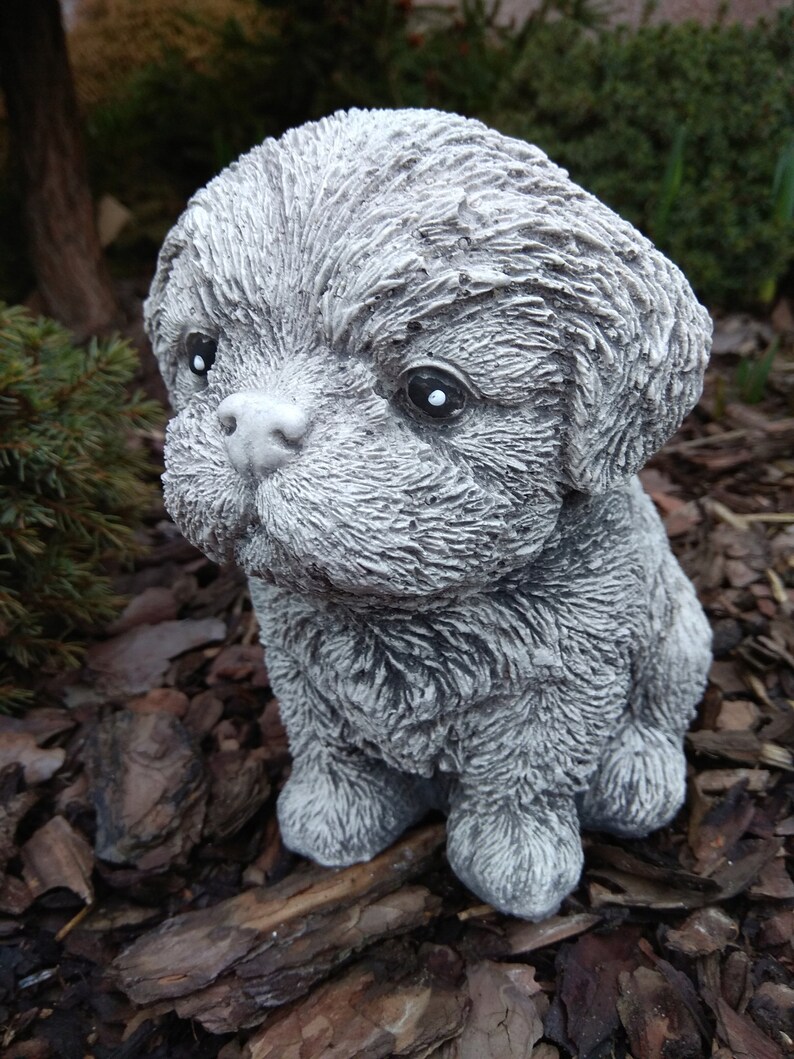 May include: A small, gray, furry, concrete statue of a dog sitting on a bed of wood chips.