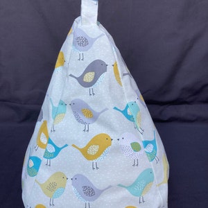 May include: A white beanbag chair with a gray, yellow, and blue bird pattern. The chair has a loop handle at the top.