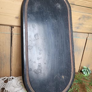 May include: Oval-shaped wooden tray with a black painted surface and a brown wooden rim. The tray has a distressed look with visible scratches and imperfections.