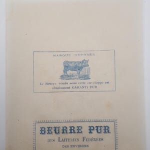 Puede incluir: Un anuncio de mantequilla antiguo en papel. La sección superior presenta una ilustración azul de un toro detrás de una valla, con el texto "MARQUE DÉPOSÉE". Debajo, el texto dice "Le Beurre vendu sous cette enveloppe est absolument GARANTI PUR". La parte inferior dice "BEURRE PUR DES LAITERIES FÉDÉRÉES DES ENVIRONS D'AVESNES".