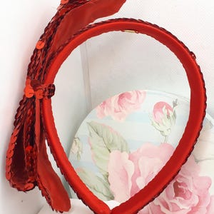Könnte beinhalten: Ein rotes Stirnband mit einer großen roten Pailletten Schleife. Das Stirnband ist aus weichem, dehnbarem Material und perfekt, um jedem Outfit einen Hauch von Glamour zu verleihen.