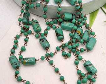 May include: A long necklace featuring turquoise-colored, rectangular beads interspersed with smaller, round beads. The rectangular beads have a mottled design with hints of yellow and black. The necklace is strung on a bronze-colored chain.
