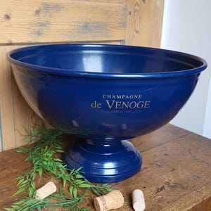 Könnte beinhalten: Ein blauer Champagnerkühler aus Metall mit einer goldenen Aufschrift "Champagne de Venogé - Depuis 1897".