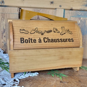 Peut inclure: Une boîte à chaussures en bois avec un couvercle à charnières. La boîte est en bois brun clair et porte une inscription noire qui dit "Boîte à Chaussures".