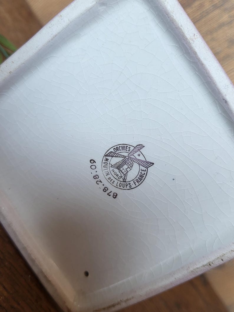 Op de afbeelding: Witte keramische plantenbak met een zwart-wit logo met de tekst "Moulin des Loups - Orchies - France" en "878.28.00".