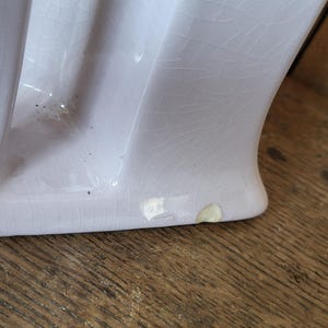 Op de afbeelding: Een close-up van de onderkant van een lichtpaarse keramische sokkelwasbak met een craquel&eacute;-glazuur. De wasbak heeft een paar chips aan de onderkant.