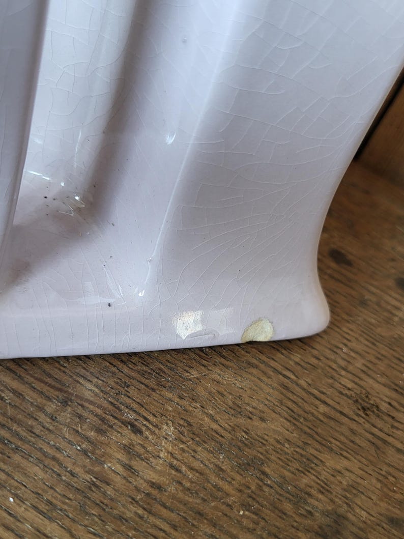 Op de afbeelding: Een close-up van de onderkant van een lichtpaarse keramische sokkelwasbak met een craquel&eacute;-glazuur. De wasbak heeft een paar chips aan de onderkant.