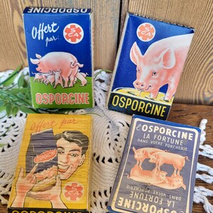 May include: Four vintage Osporcine playing card decks. The decks feature illustrations of pigs and text in French. The decks are blue, yellow, and white, with the text "Offert par" and "54 Cartes".