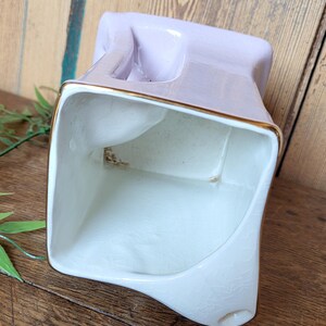 Op de afbeelding: Een witte keramische plantenpot met een lavendelglazuur en gouden rand. De pot heeft een vierkante vorm met een uniek, asymmetrisch ontwerp.