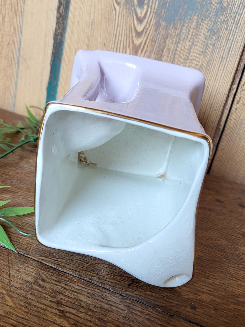 Op de afbeelding: Een witte keramische plantenpot met een lavendelglazuur en gouden rand. De pot heeft een vierkante vorm met een uniek, asymmetrisch ontwerp.