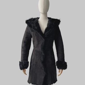 May include: A black coat featuring a hood, long sleeves with fur-trimmed cuffs, and a front button closure. The garment is constructed with a smooth, matte exterior finish and is lined with black fur along the hood, collar, and front opening.