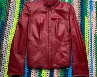 May include: A red leather jacket with a zip fastening and long sleeves. The jacket has a stand-up collar and two pockets.