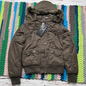 Peut inclure: Veste bombardier marron avec capuche doublée de fausse fourrure. La veste a plusieurs poches, une fermeture éclair et des poignets et ourlets côtelés. L'étiquette indique "E-Night Fashion".
