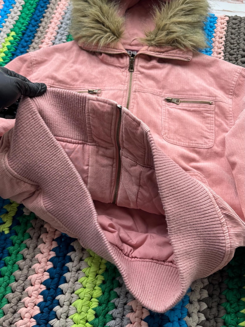 May include: A pink corduroy jacket with a faux fur hood. The jacket has a zipper closure and two pockets.
