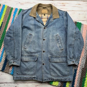 May include: A light blue denim jacket with a corduroy collar and a plaid lining. The jacket has two large pockets on the front and a button closure.