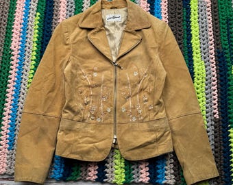 May include: A tan suede jacket with a zipper closure and floral embroidery. The jacket has a label that reads "aviano".
