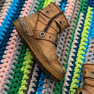 May include: A pair of brown leather ankle boots with multiple buckles and metal eyelets. The boots have a zipper on the side and a chunky sole.