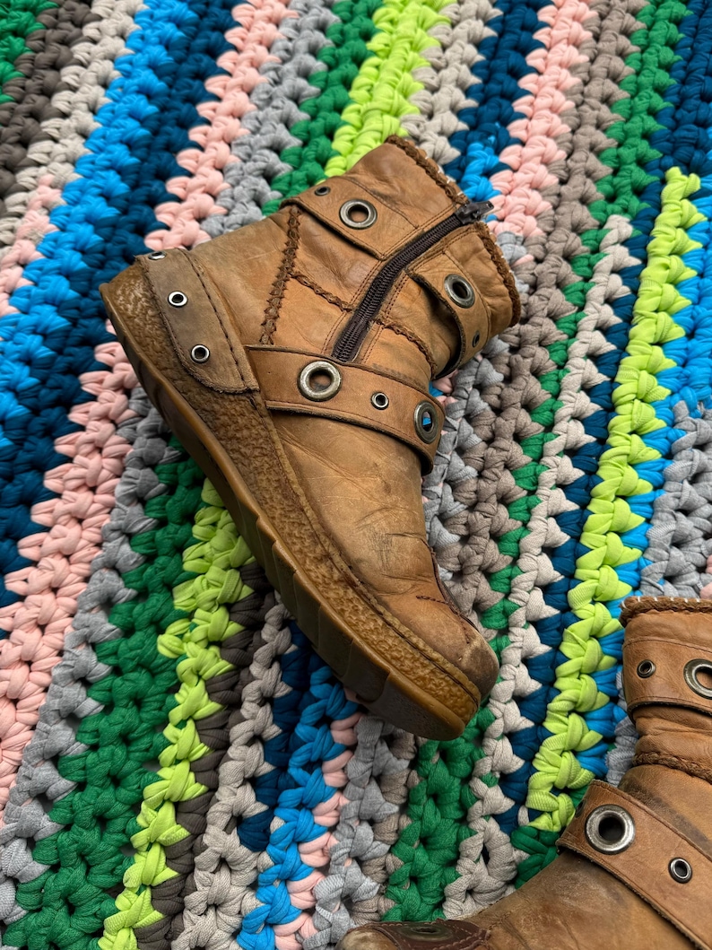 May include: A pair of brown leather ankle boots with multiple buckles and metal eyelets. The boots have a zipper on the side and a chunky sole.