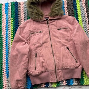 May include: A pink corduroy jacket with a faux fur lined hood. The jacket has a zipper closure and multiple pockets.
