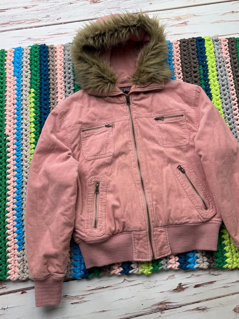May include: A pink corduroy jacket with a faux fur lined hood. The jacket has a zipper closure and multiple pockets.