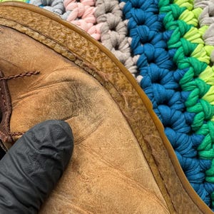 May include: Close-up of the brown leather sole of a shoe. The leather is worn and has a textured surface. The sole is stitched to the upper part of the shoe.