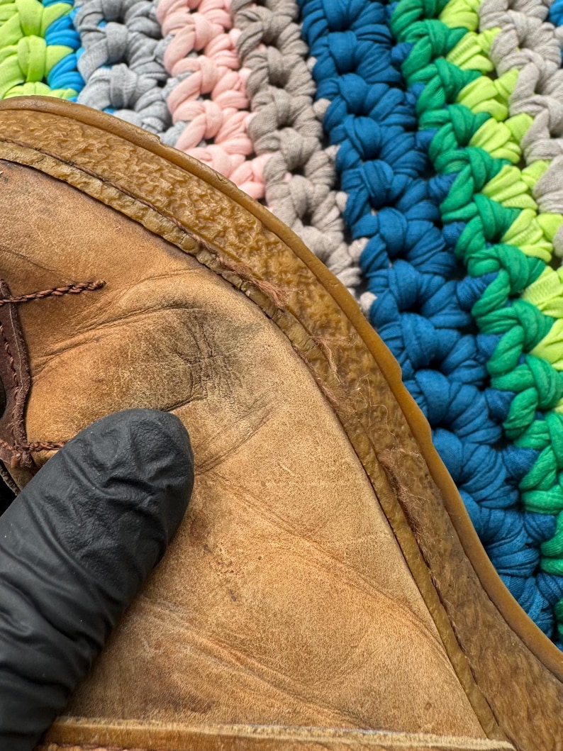 May include: Close-up of the brown leather sole of a shoe. The leather is worn and has a textured surface. The sole is stitched to the upper part of the shoe.