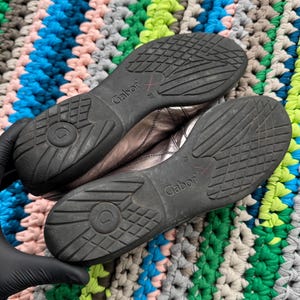May include: A pair of silver leather shoes with black soles. The shoes have the brand name "Gabor" printed on the side.