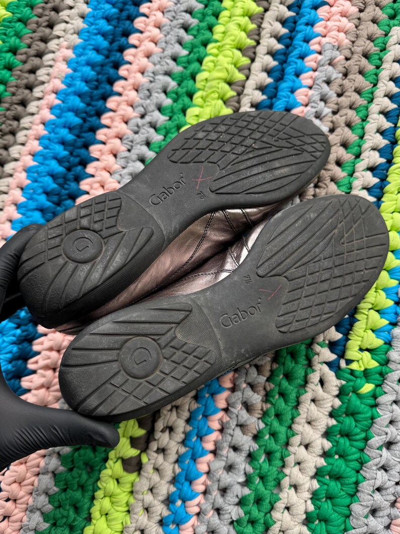 May include: A pair of silver leather shoes with black soles. The shoes have the brand name "Gabor" printed on the side.