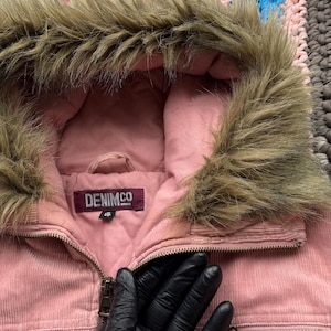 May include: Pink corduroy jacket with a faux fur lined hood. The jacket has a zipper closure and two pockets on the front. The label on the jacket reads "DENIMCO 38".