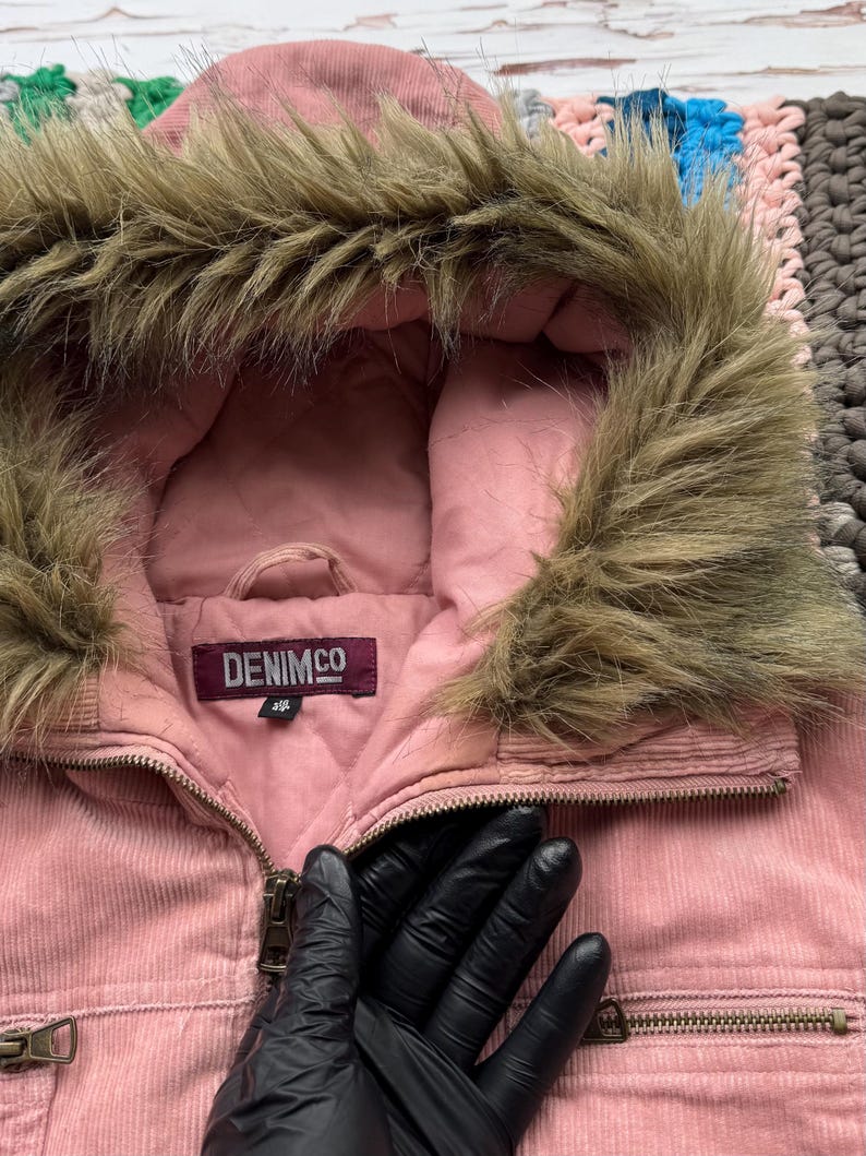 May include: Pink corduroy jacket with a faux fur lined hood. The jacket has a zipper closure and two pockets on the front. The label on the jacket reads "DENIMCO 38".