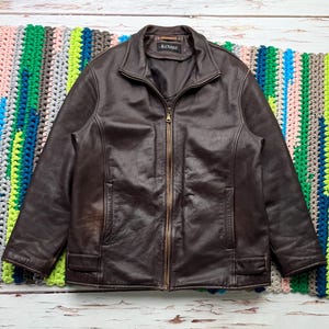May include: A brown leather jacket with a zipper closure and a B.Coast label. The jacket has two pockets on the front and a ribbed collar.