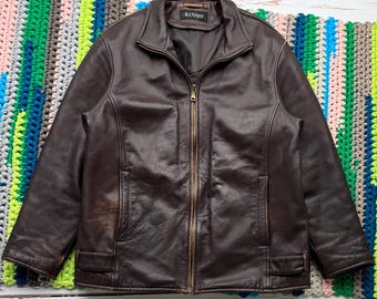 Può includere: Una giacca di pelle marrone con chiusura a zip e un'etichetta B.Coast. La giacca ha due tasche sul davanti e un colletto a costine.
