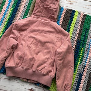 May include: A pink corduroy jacket with a faux fur lined hood. The jacket has a zipper closure and a ribbed waistband.
