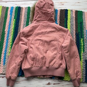 May include: A pink corduroy bomber jacket with a faux fur lined hood. The jacket has a ribbed hem and cuffs.