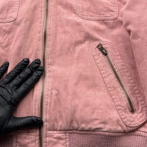 May include: A pink corduroy jacket with a zipper closure and multiple pockets. The jacket has a ribbed waistband and a soft, textured fabric.