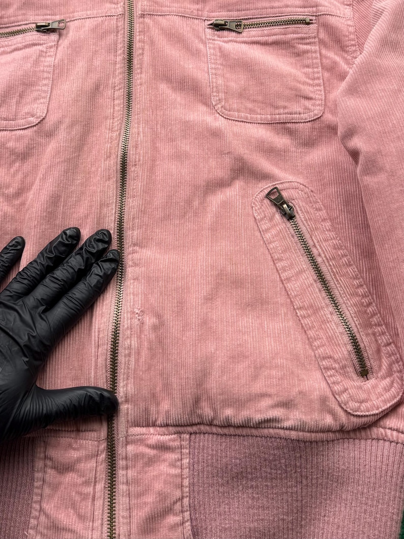 May include: A pink corduroy jacket with a zipper closure and multiple pockets. The jacket has a ribbed waistband and a soft, textured fabric.