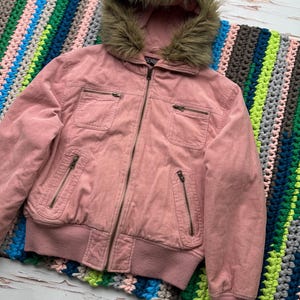 May include: A pink corduroy jacket with a faux fur lined hood. The jacket has a zipper closure and multiple pockets.