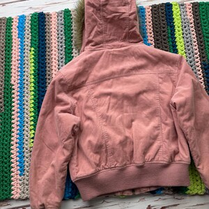 May include: A pink corduroy jacket with a faux fur lined hood. The jacket has a zipper closure and a ribbed hem and cuffs.