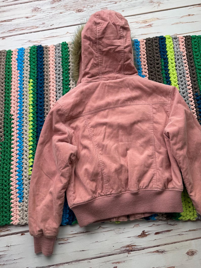 May include: A pink corduroy jacket with a faux fur lined hood. The jacket has a zipper closure and a ribbed hem and cuffs.