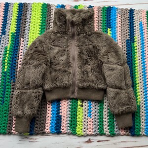 May include: A brown faux fur jacket with a zipper closure and a high collar. The jacket has a cropped length and ribbed cuffs and hem.