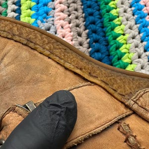 May include: Close-up of a brown leather boot with a seam along the top edge. The boot is worn and has a dark brown leather sole.