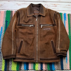 May include: A brown leather jacket with a zipper closure and multiple pockets. The jacket has a suede collar and white stitching.