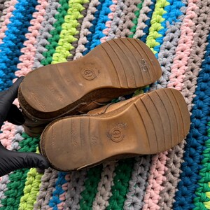 May include: A pair of brown leather boots with a thick rubber sole. The boots have a brown leather upper with a stitched seam around the ankle. The boots have a brown leather tongue with a brown leather lace.