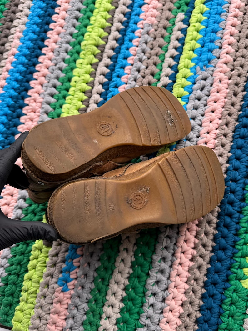 May include: A pair of brown leather boots with a thick rubber sole. The boots have a brown leather upper with a stitched seam around the ankle. The boots have a brown leather tongue with a brown leather lace.