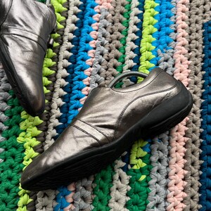 May include: A pair of silver leather shoes with black soles. The shoes are on a colorful crocheted rug.