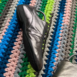 May include: A pair of silver leather shoes with a zipper on the side. The shoes are on a colorful crocheted rug.