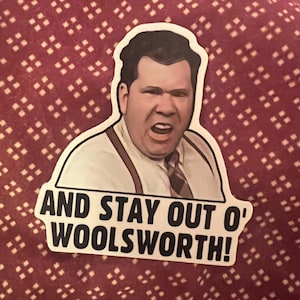 May include: A sticker featuring a cartoon image of a man with a serious expression. The sticker has the text "AND STAY OUT O' WOOLSWORTH!" printed on it.
